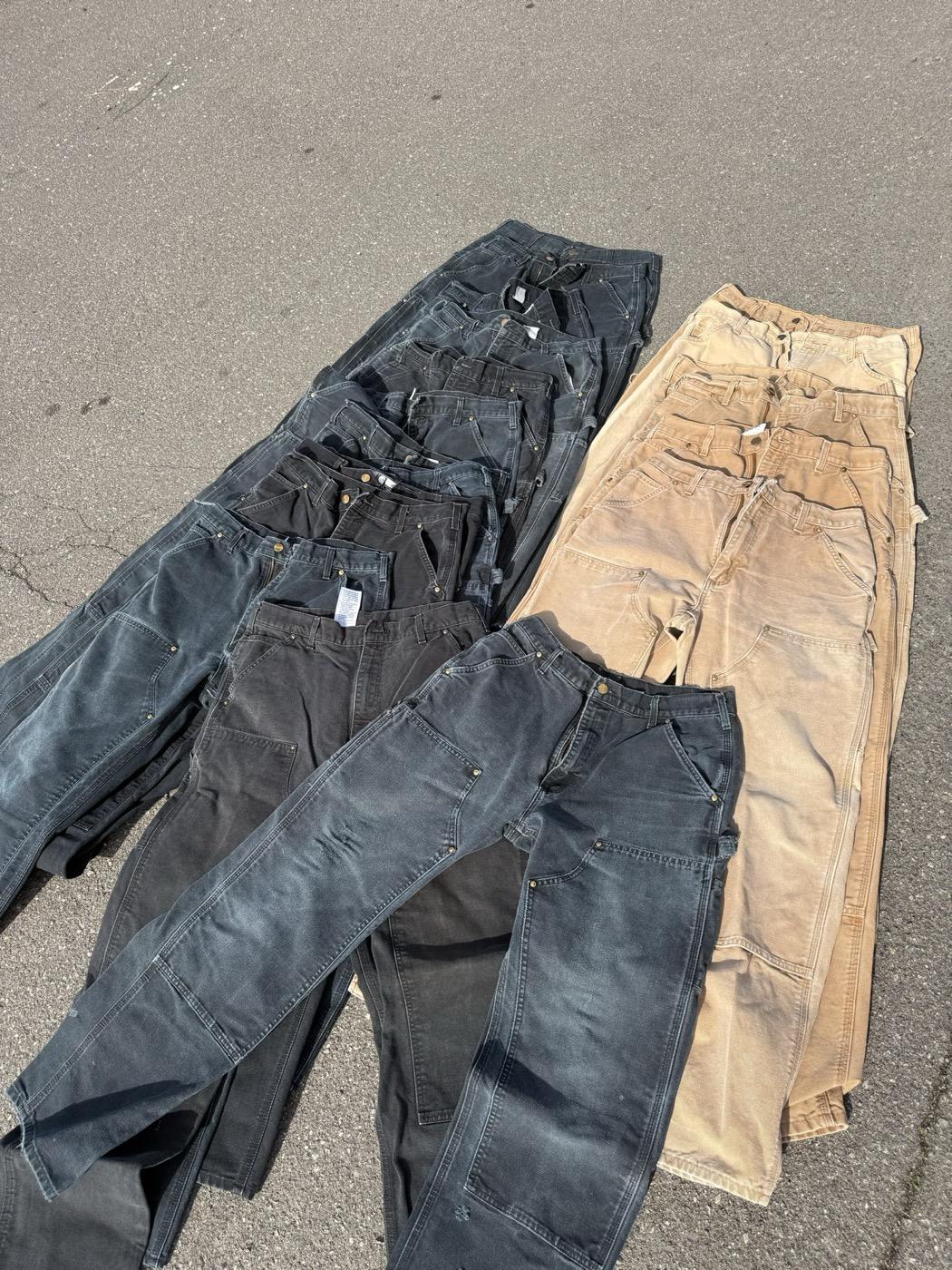 Worn black and tan duck canvas double-knee work pants laid out in rows on pavement