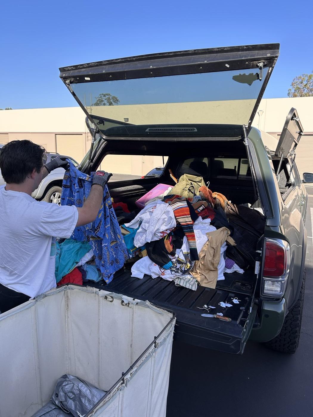 A pickup bed full of vintage clothing being unloaded by hand into a canvas sorting cart