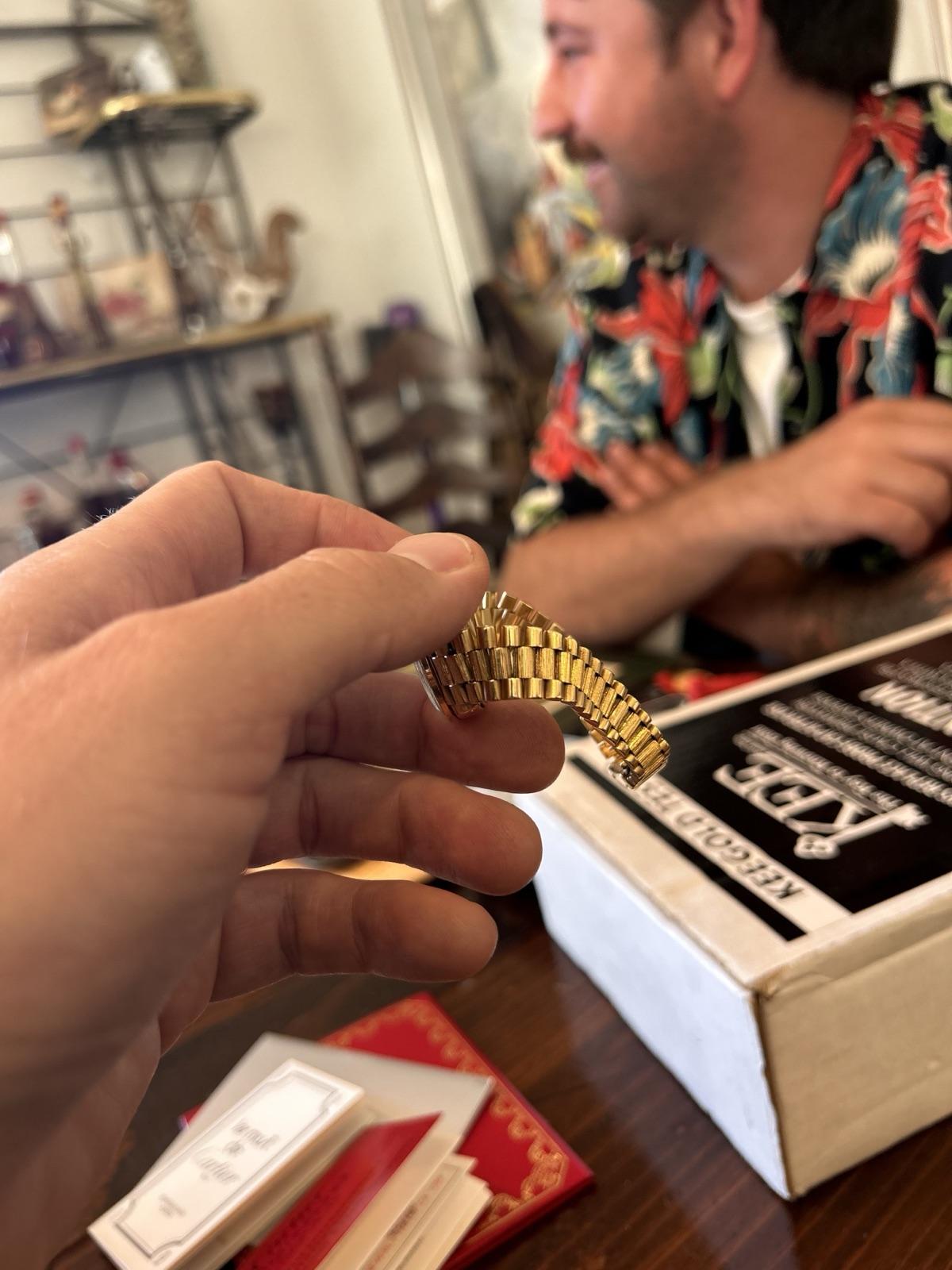 A vintage watch bracelet being examined hand to hand at a seller's table, Jake smiling mid-conversation with the seller in the background
