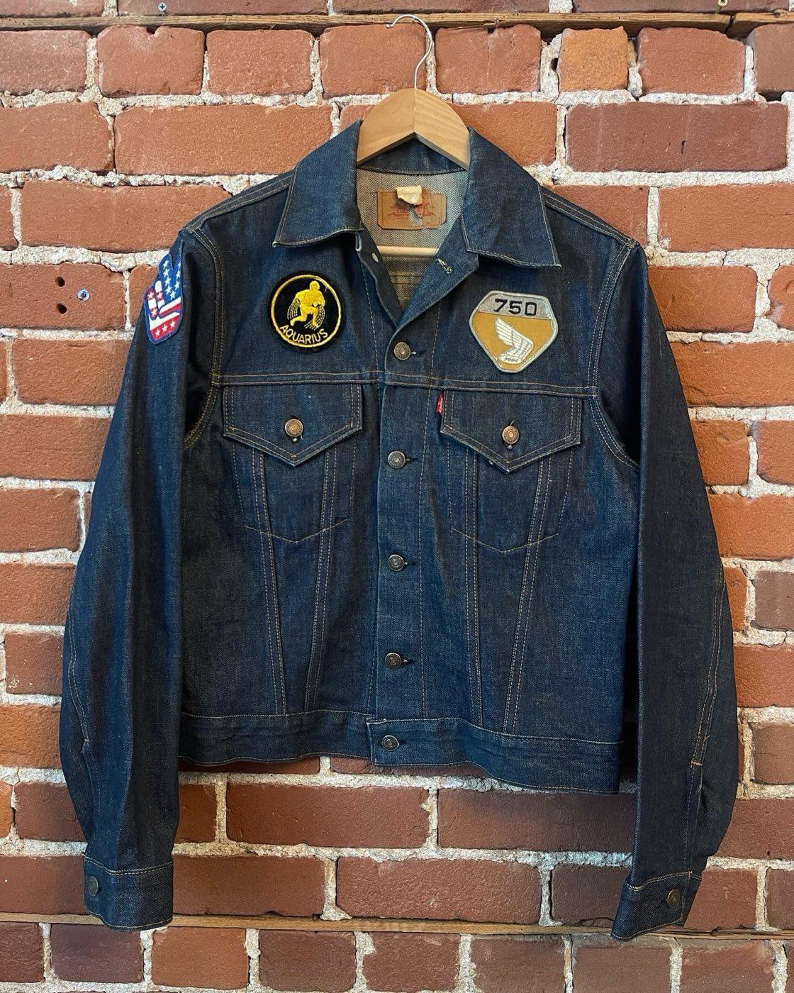 Dark early 1970s Levi's trucker jacket on a hanger with period Aquarius, Honda 750, and flag patches