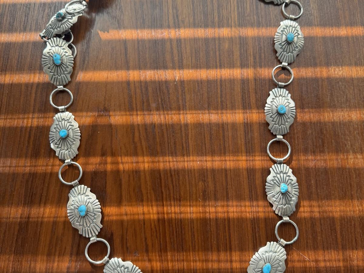 Stamped silver concho link belt with turquoise stones, conchos joined by silver rings, laid on a wood table