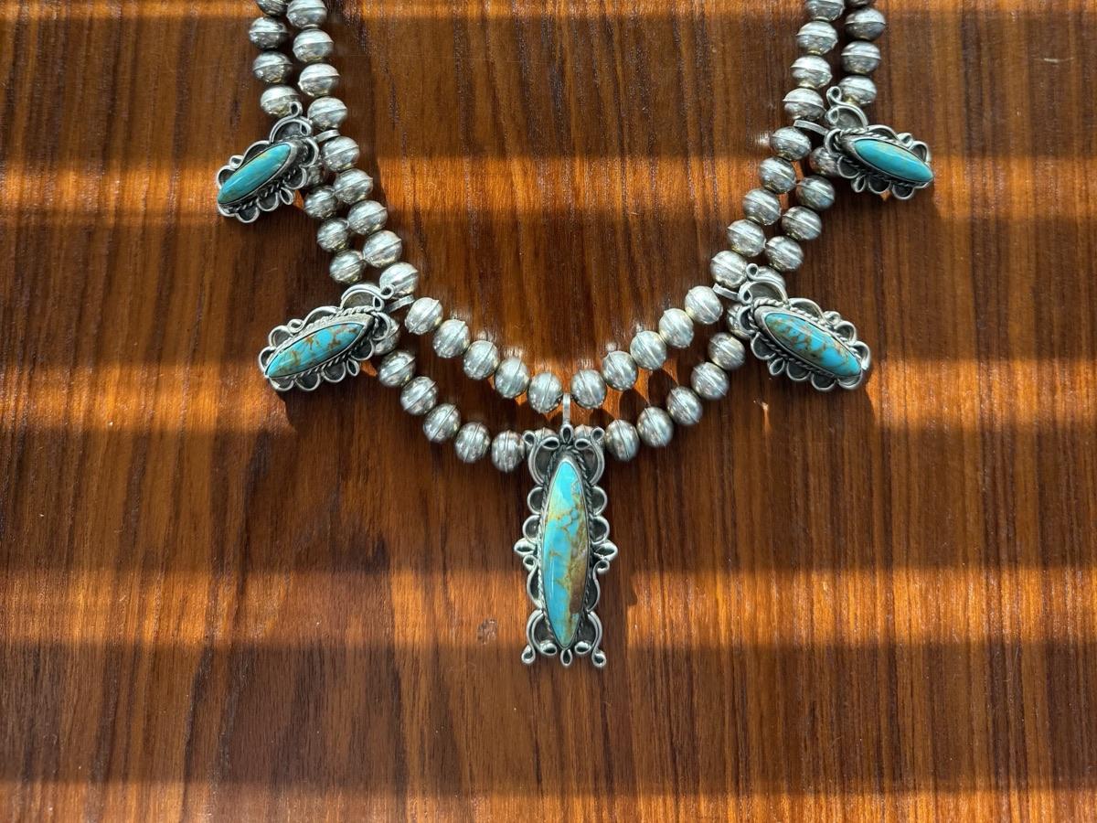 Five stone turquoise and sterling silver necklace with bench beads and a scalloped center drop, laid on a wood table