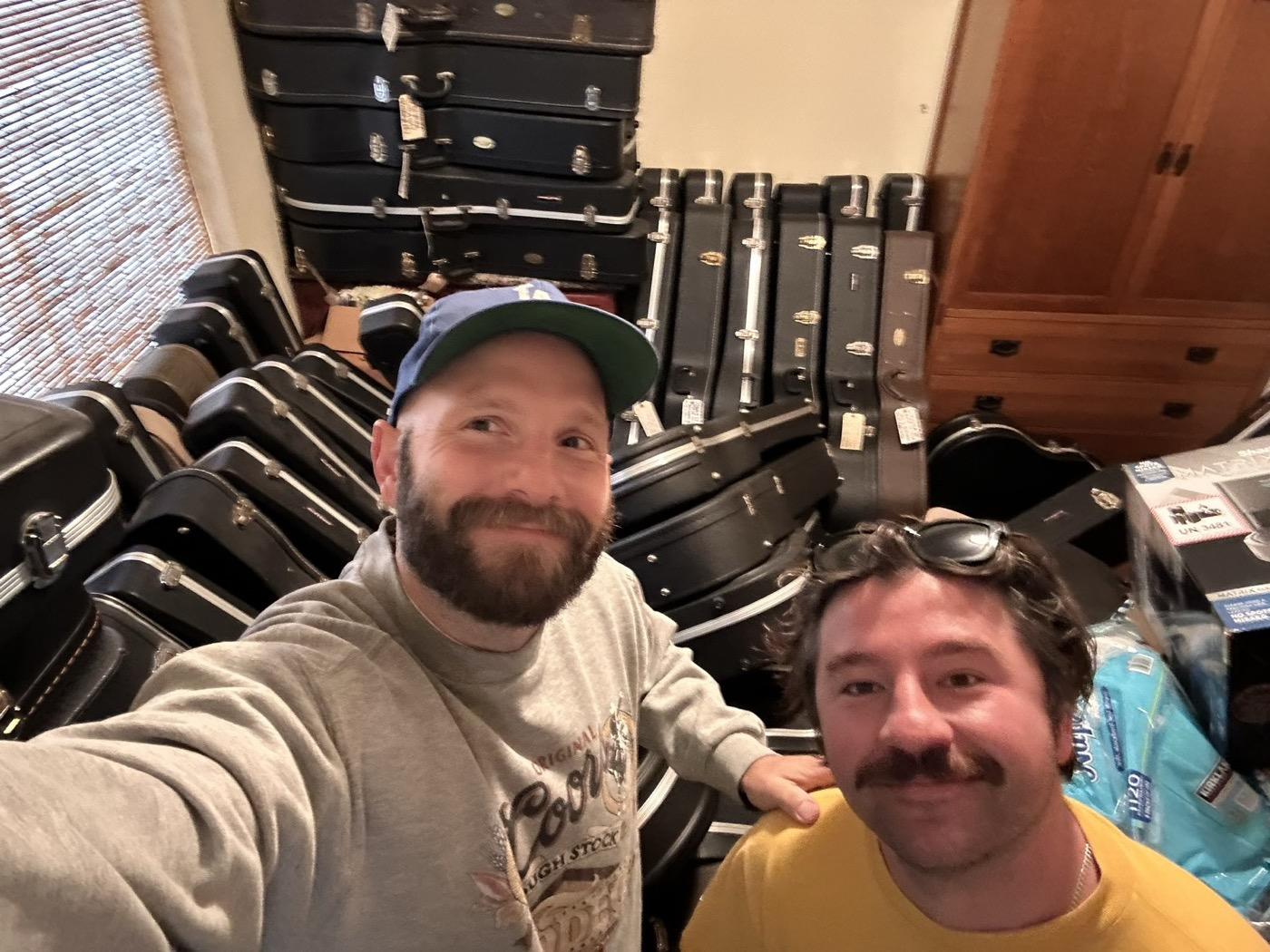 Sam and Jake of California Vintage Buyers at a house call, surrounded by a wall of guitar cases they are buying