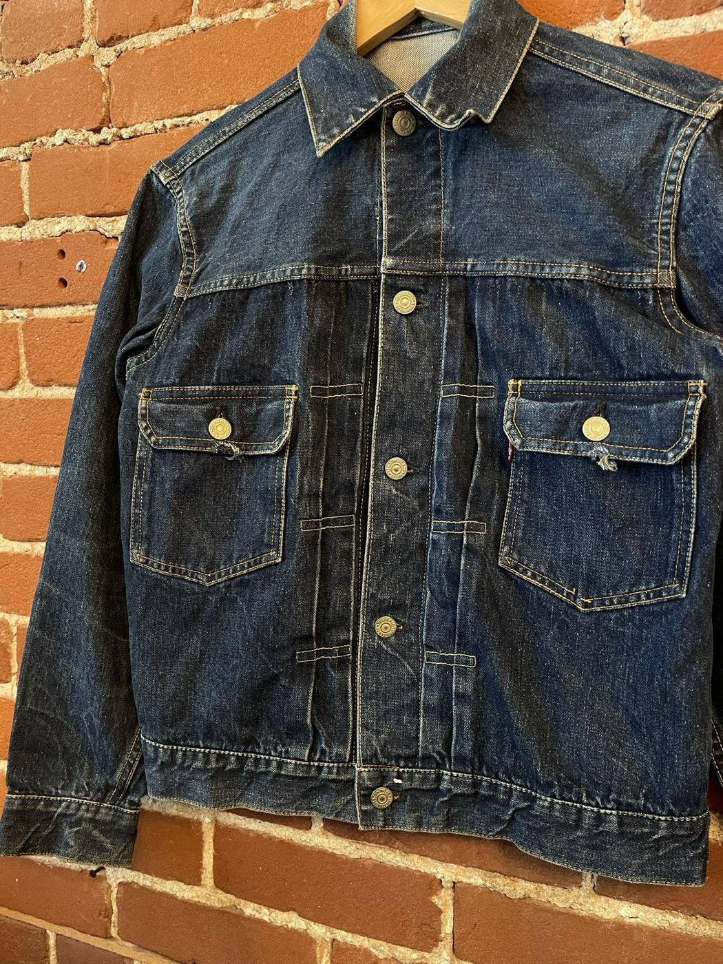 Worn Levi's Type 2 denim jacket with two pleated chest pockets, laid against a brick wall