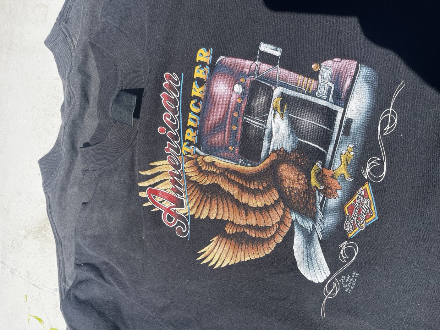 Black American Trucker t-shirt with an eagle and a semi truck, the small print beside the graphic reading 1987 3D Emblem Ft. Worth TX