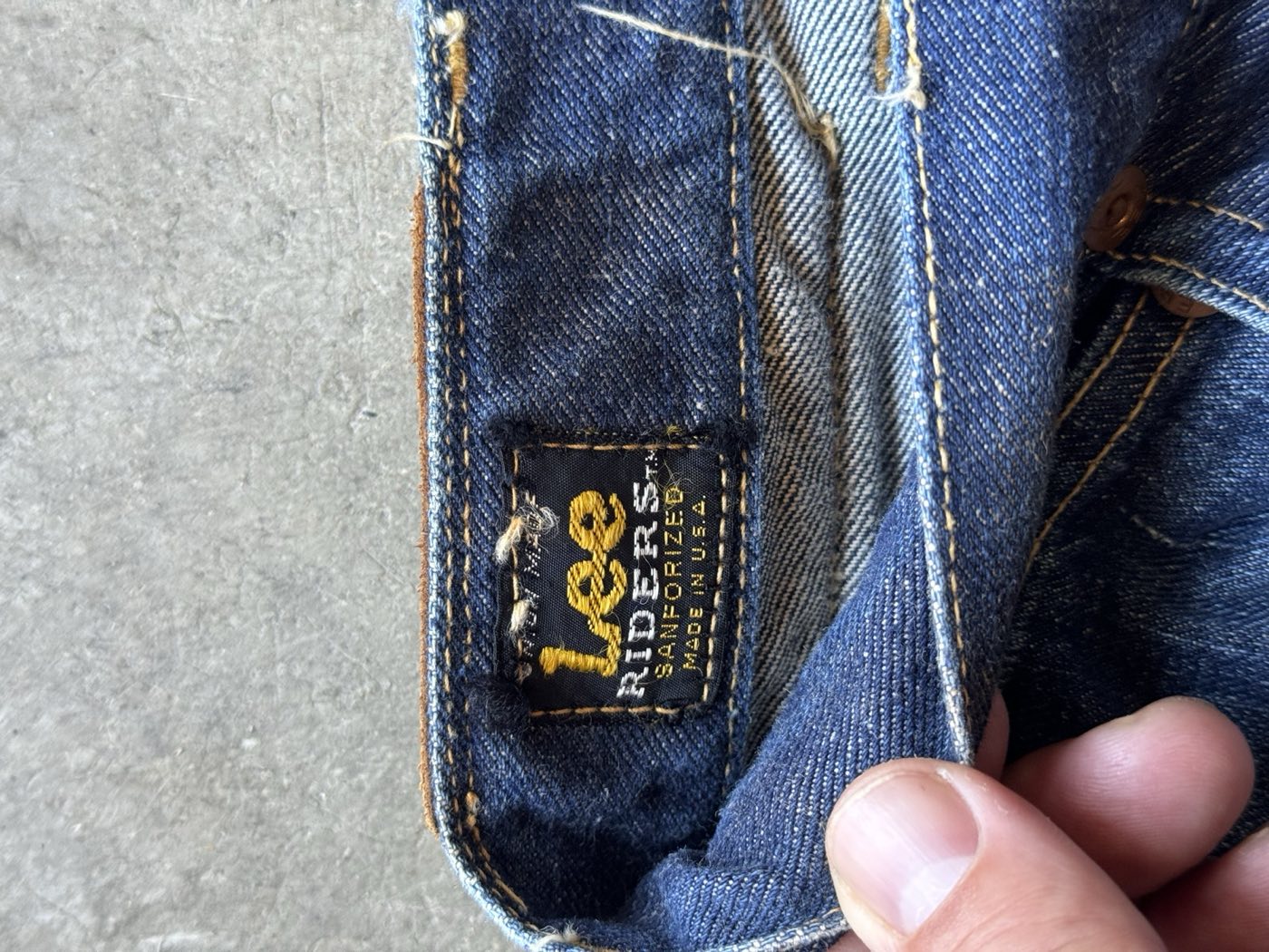Close-up of a black and gold Lee Riders waistband tag inside vintage jeans reading Union Made, Lee Riders TM, Sanforized, Made in U.S.A., with the leather patch visible on the outside of the waistband