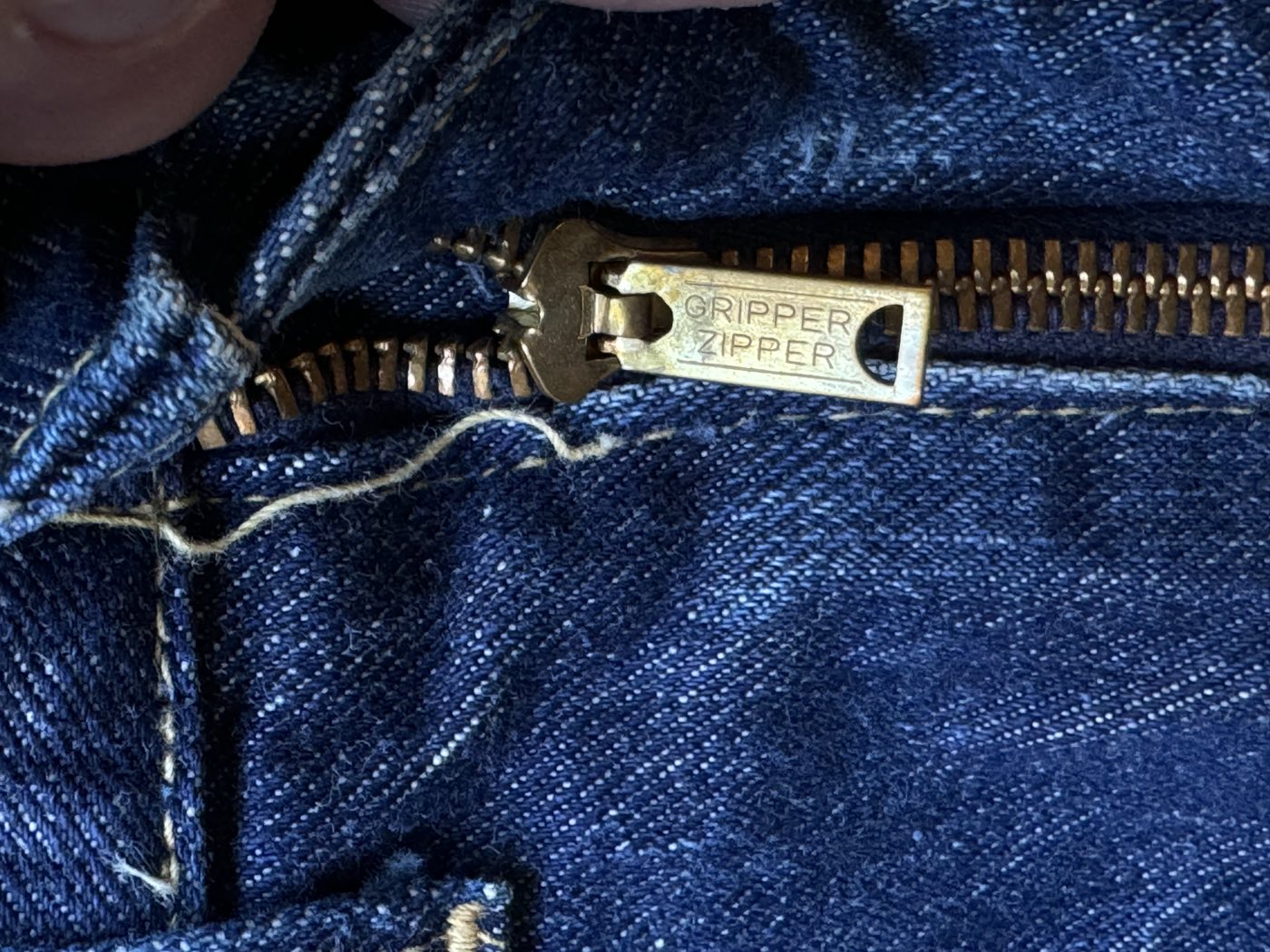 Close-up of a brass zipper pull stamped Gripper Zipper on the fly of vintage Lee Riders jeans, with brass teeth and yellow contrast stitching