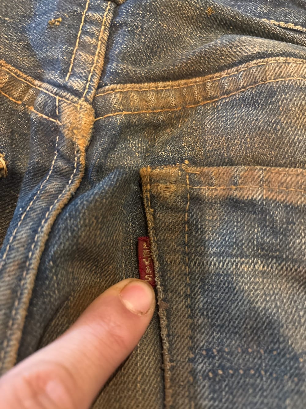Finger lifting the red tab on the back pocket of worn vintage Levi's jeans, LEVI'S stitched in white capital letters