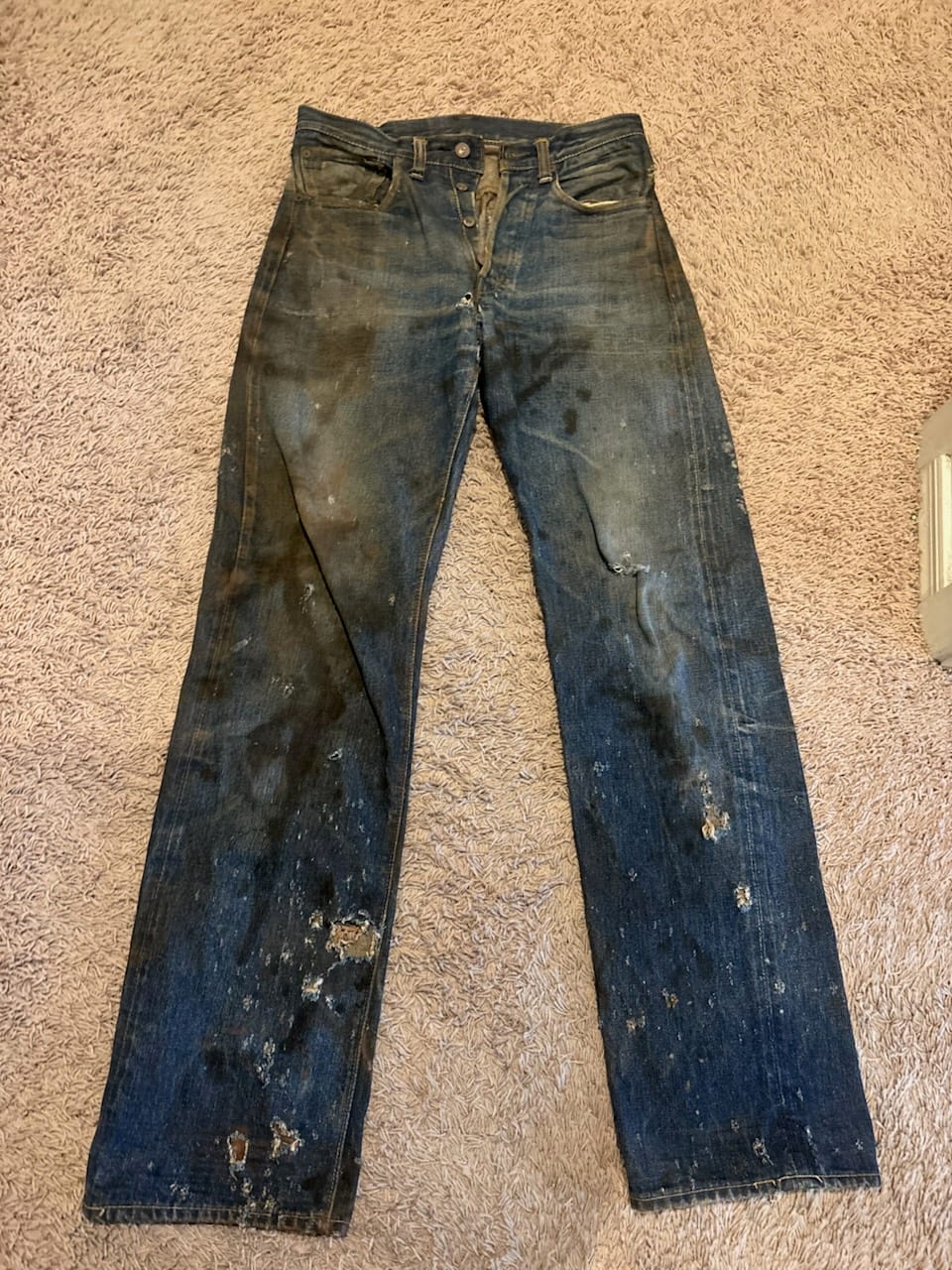Full front view of heavily soiled vintage Levi's jeans laid flat, button fly, dark staining and holes down both legs