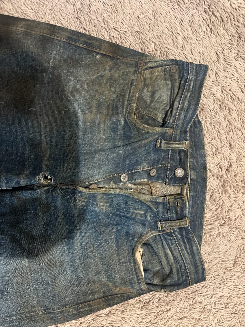 Waist and button fly detail of vintage Levi's jeans with exposed metal buttons and heavy staining