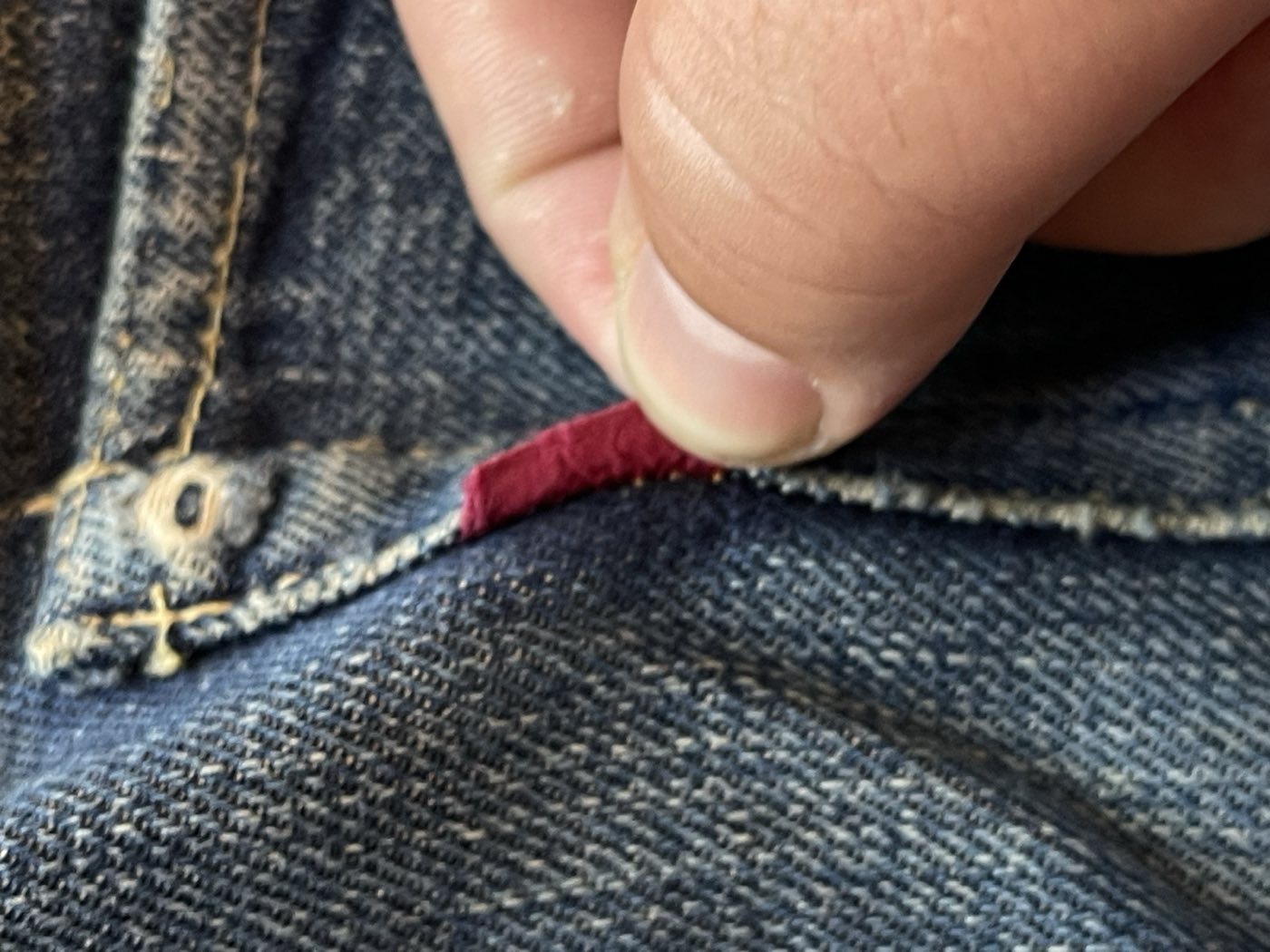 Fingers folding back the red tab on a pair of 1940s Levi's 501XX jeans showing the blank reverse side