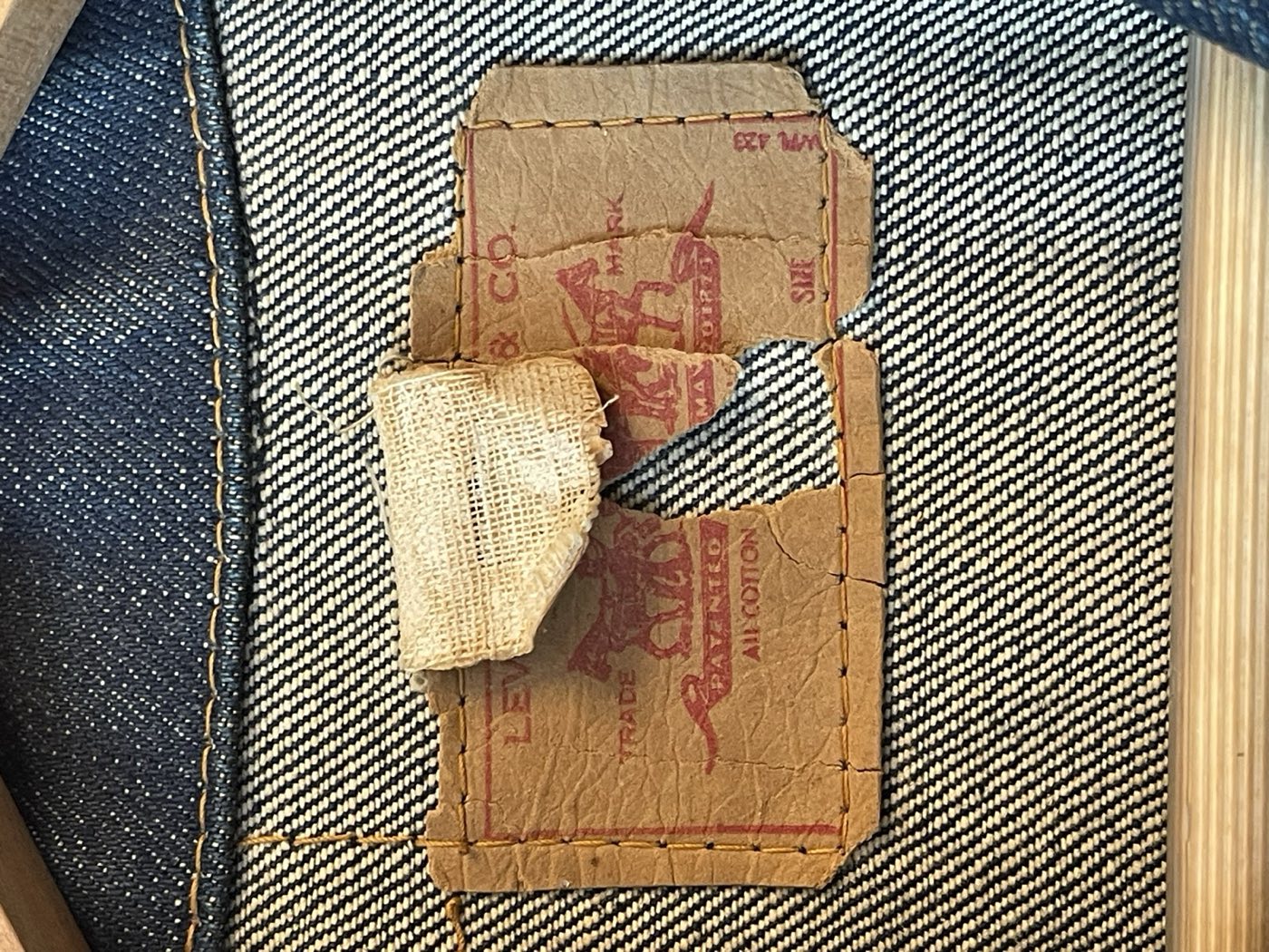 Torn Levi's paper patch on dark denim, red two horse trademark and the words all cotton still visible