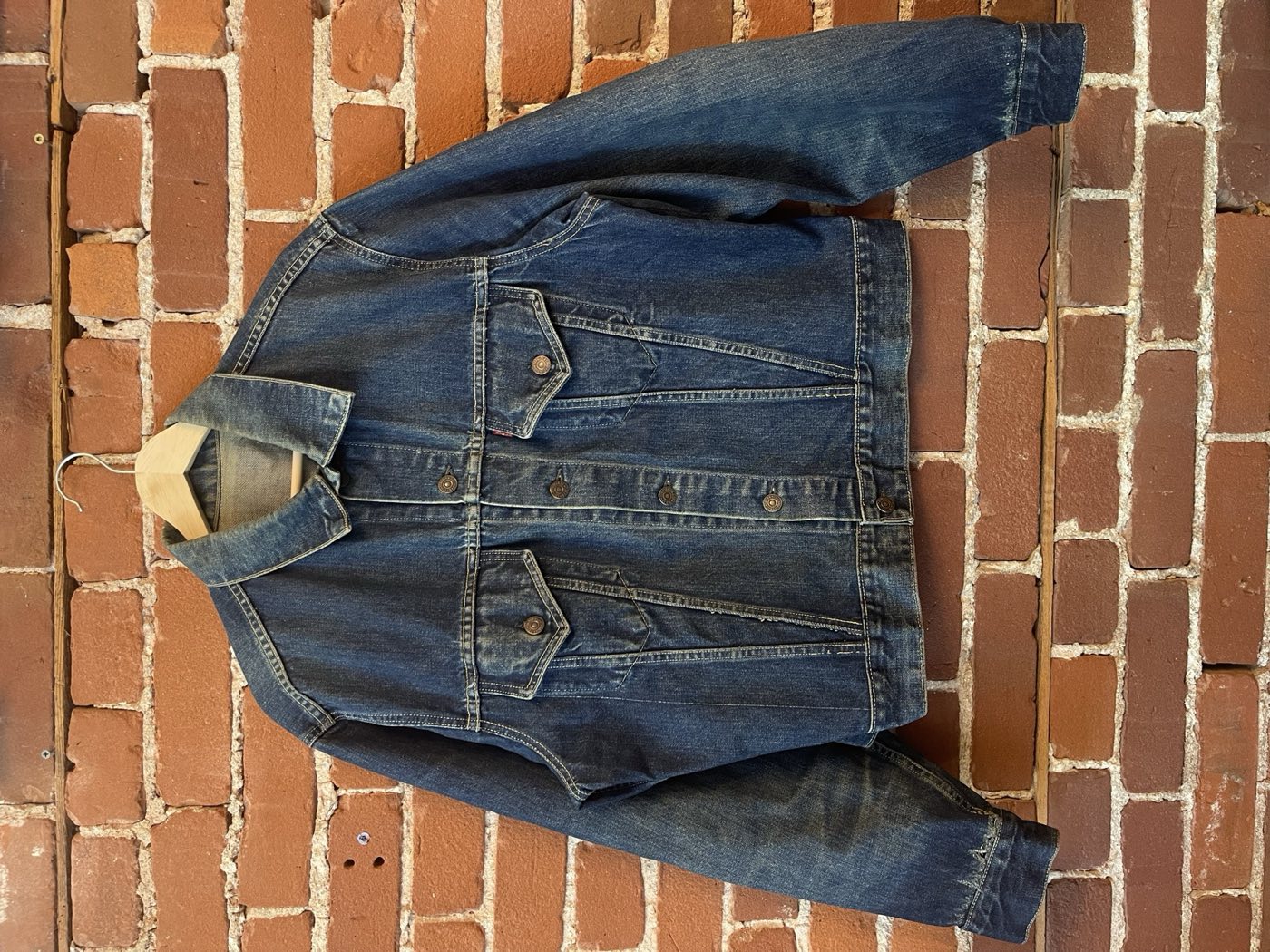 1960s Levi's 557XX Type 3 Big E trucker jacket with strong contrast fade, hanging against a brick wall