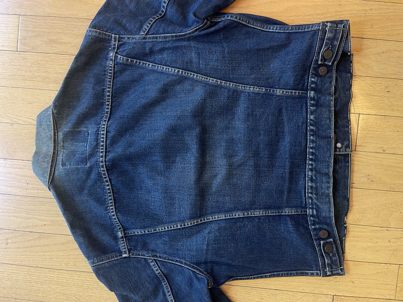 Back of a dark Levi's Type 3 trucker jacket showing the waist adjuster tabs and the pale rectangle where the patch was removed