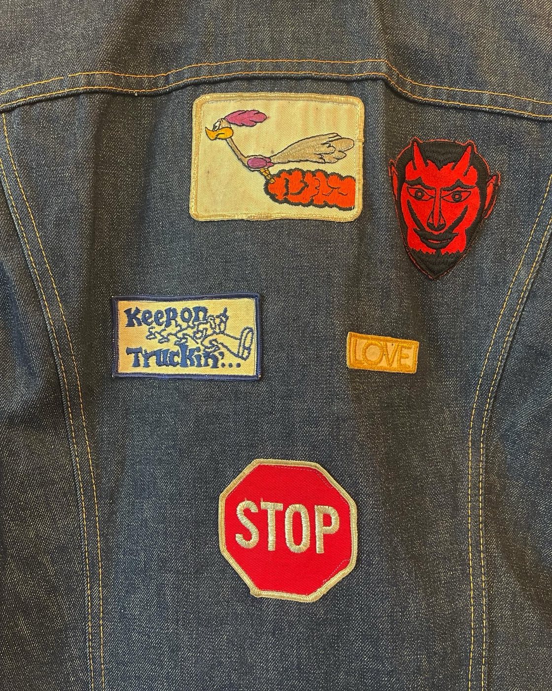 Close up of period 1970s patches on denim including a road runner cartoon, red devil head, Keep on Truckin slogan, and a LOVE patch