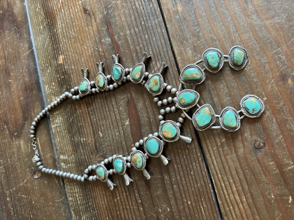 Squash blossom necklace with green turquoise stones laid on a wood table for evaluation