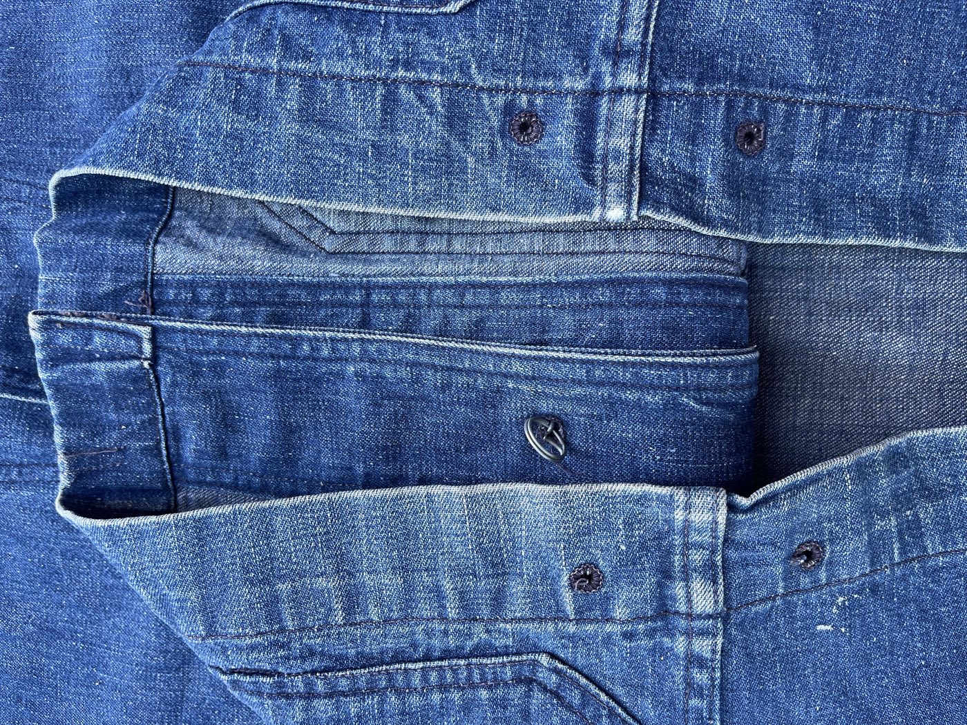Close view of the shawl collar and front of a WWII US Navy denim jacket showing dark round embossed buttons, one button ring, and the lighter undyed weave of the denim on the reverse