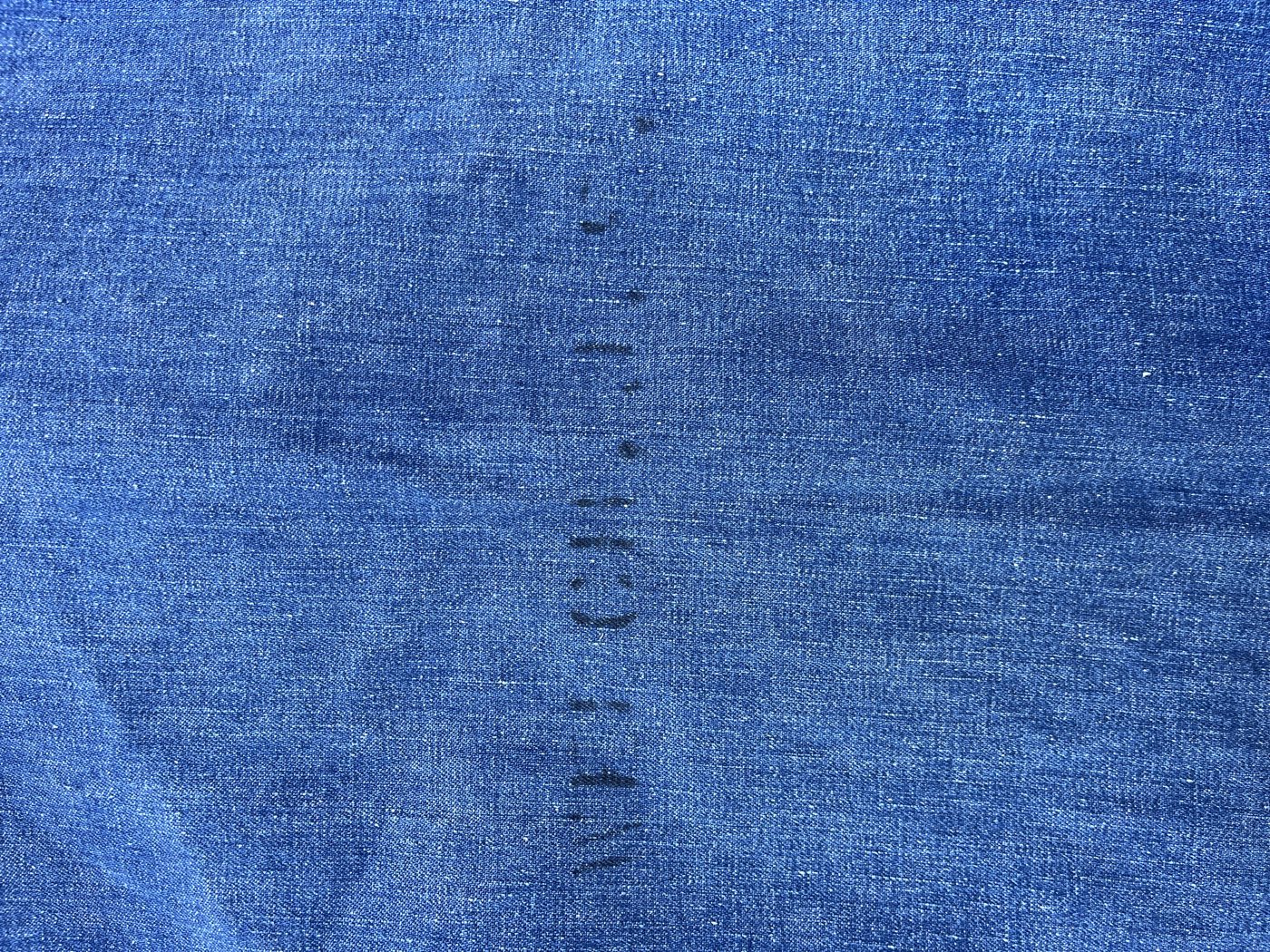 Close view of a faded black stencil on indigo denim, a column of letters running down the back of a WWII US Navy jacket, partly worn into the weave